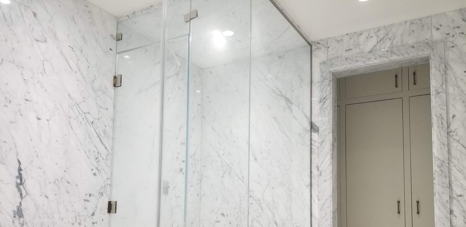 Anajur Staten Island bathroom: Carrara marble walls, frameless glass enclosure, marble-clad doorway.