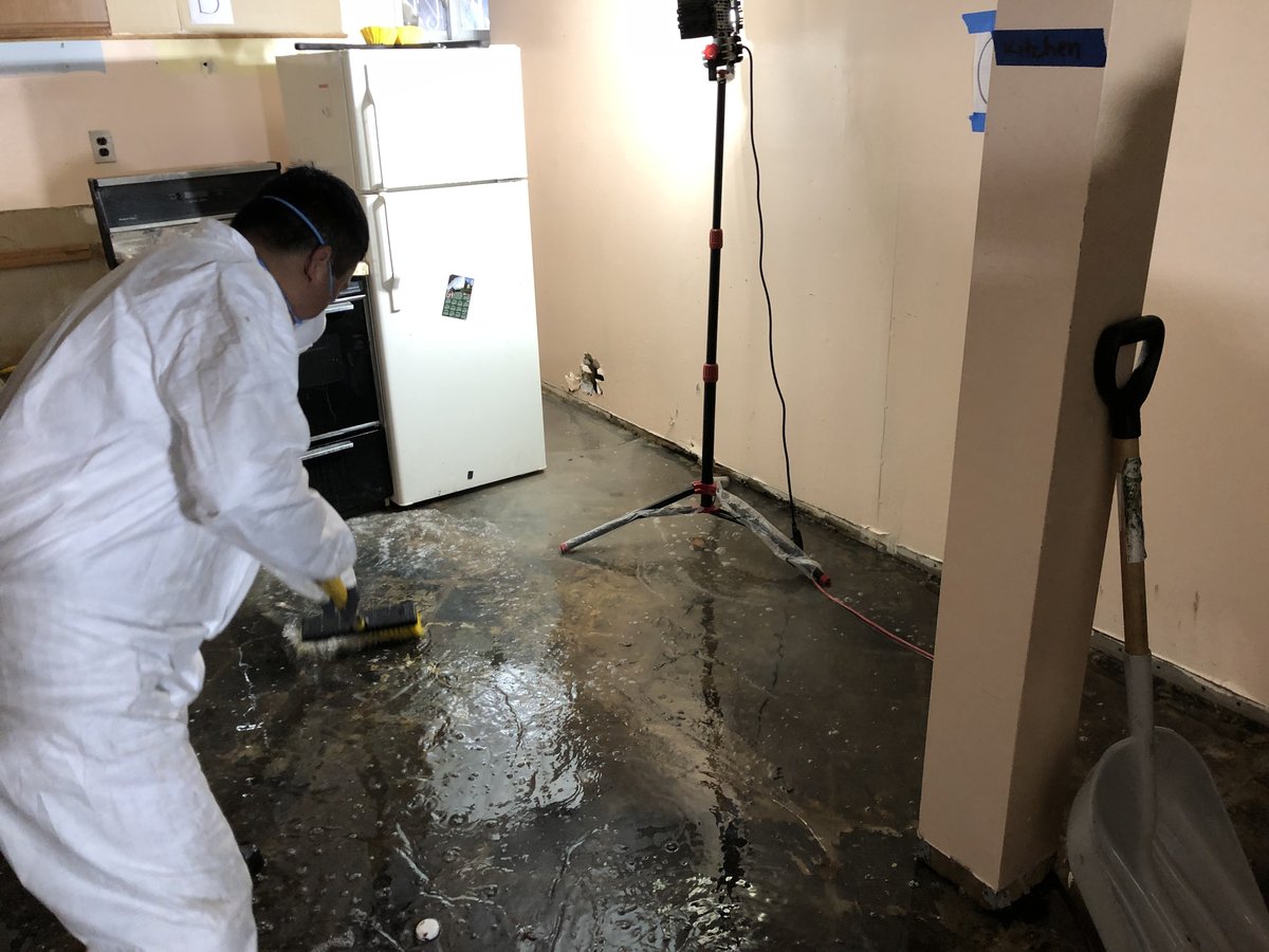 Anajur crew member in full PPE performing push-broom mechanical agitation on a wet kitchen floor in Staten Island.