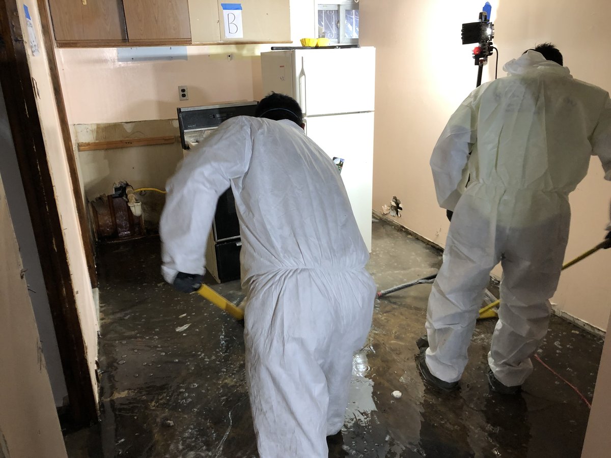 Two Anajur crew members in full PPE coordinating mitigation work in a Staten Island kitchen with documentation tape.